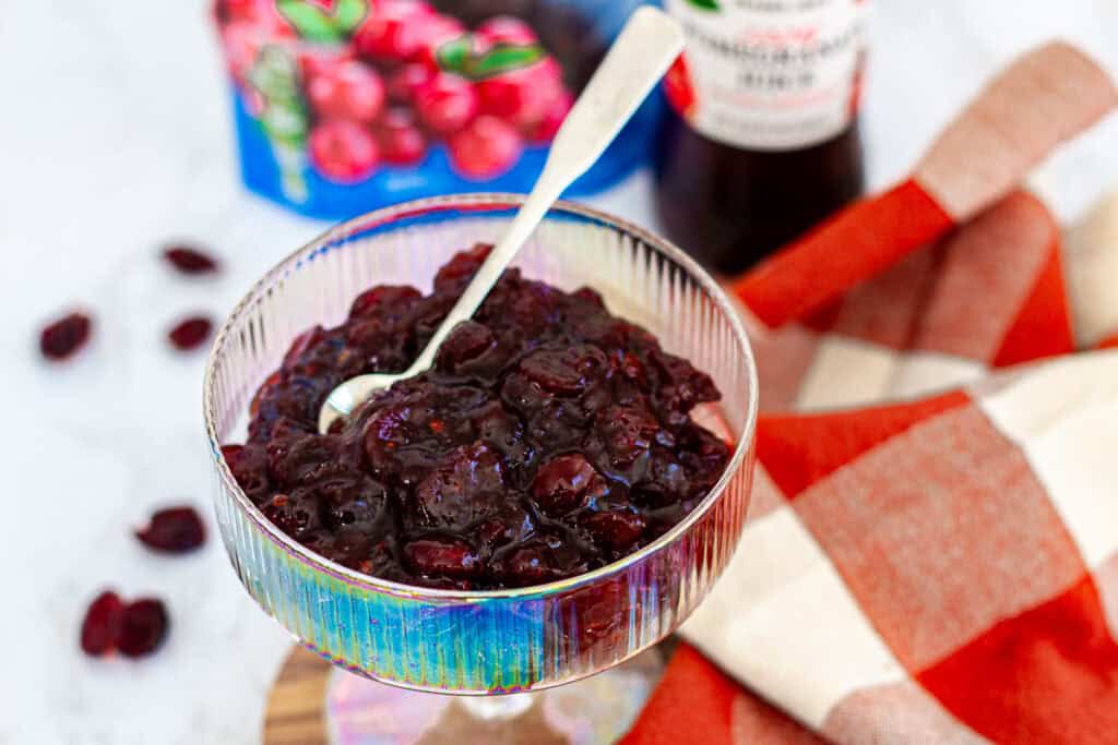 Bowl of homemade cranberry sauce with dried cranberries placed on a wooden coaster, ready to serve.