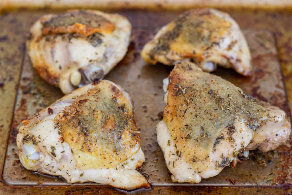 Golden roasted chicken thighs on a sheet pan after baking with dried herb butter.