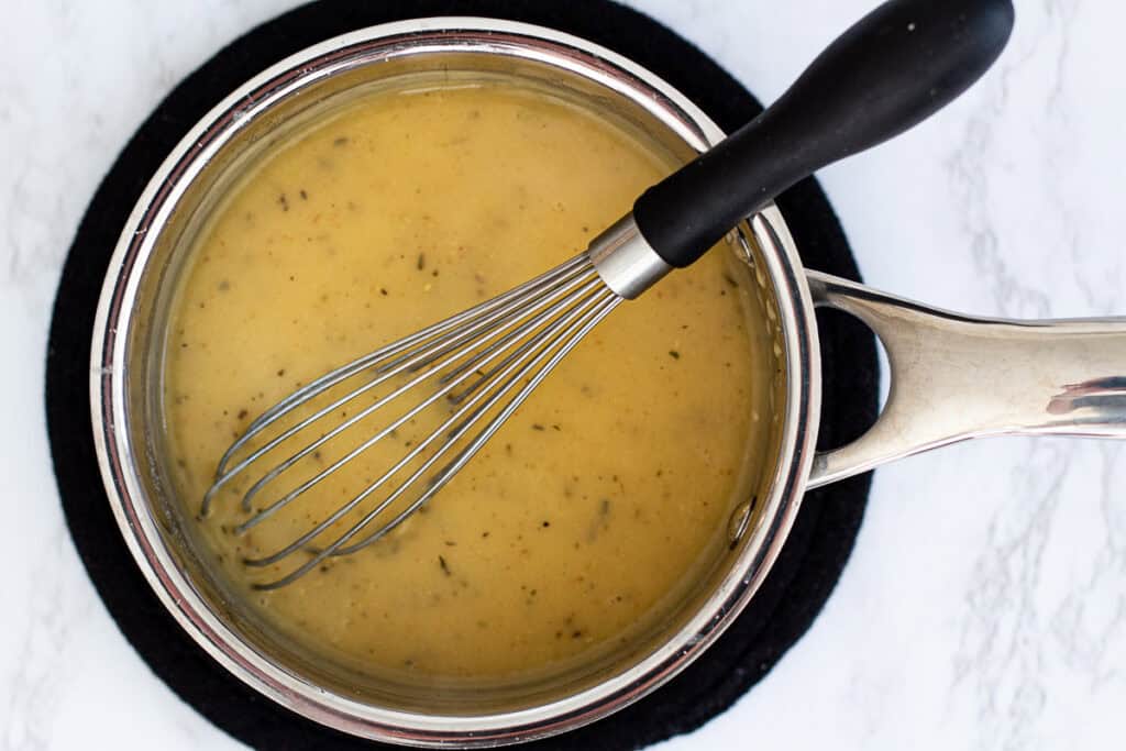 Saucepan with smooth golden gravy whisked from chicken drippings, butter, and flour.