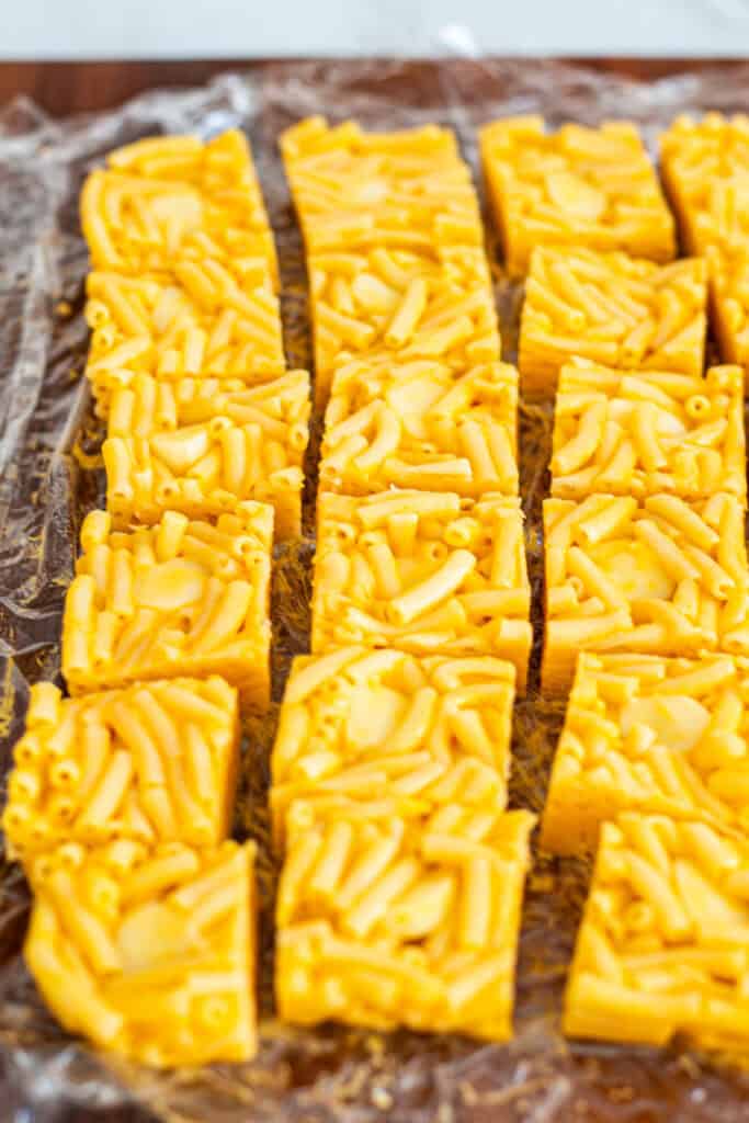 Sliced mac and cheese squares on plastic wrap, ready to be breaded for mac and cheese bites.