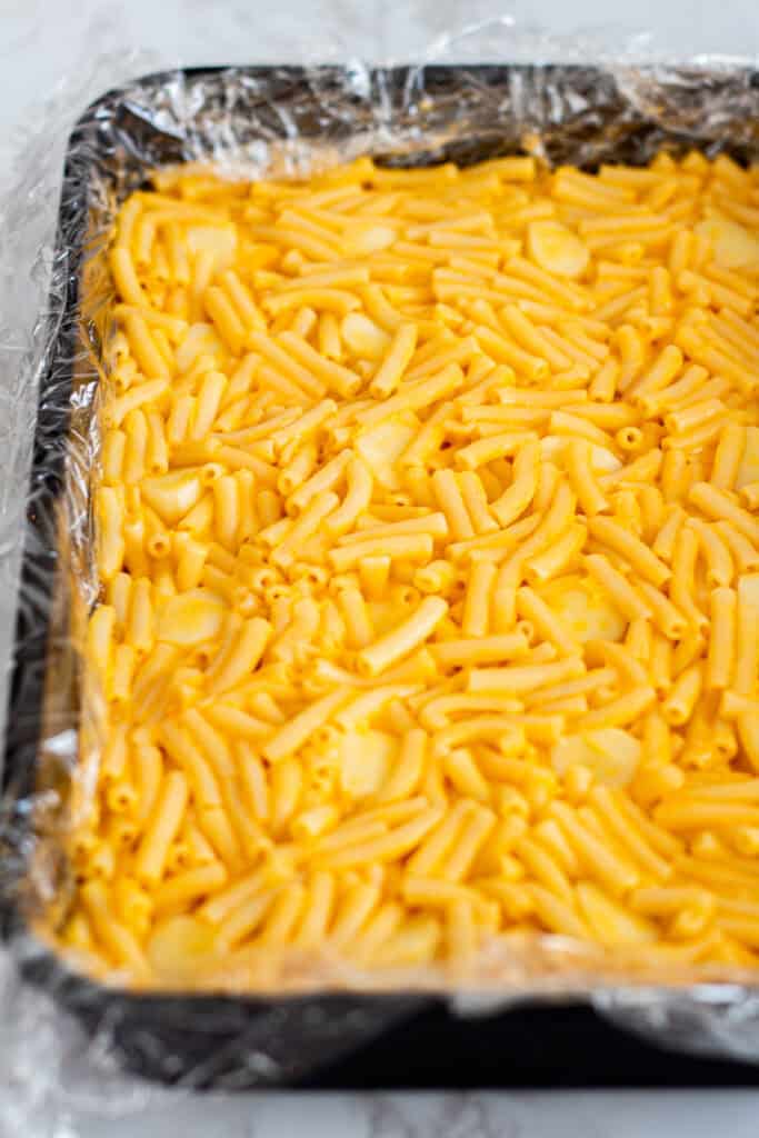Full pan of chilled boxed mac and cheese lined with plastic wrap, firm and ready to slice into squares.