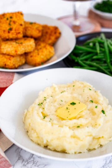Bowl of creamy mashed potatoes with butter, served with green beans and mac and cheese bites