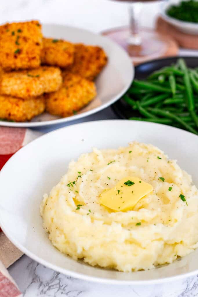 Bowl of creamy mashed potatoes with butter, served with green beans and mac and cheese bites