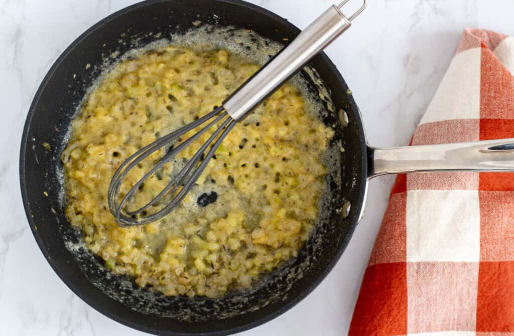 veggie and roux cooking in a skillet with a whisk, the start of Thanksgiving gravy.