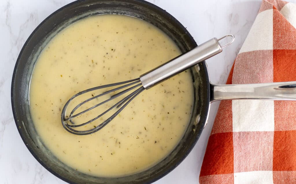 Pan of smooth golden gravy whisked and ready to serve with stuffed chicken breast.