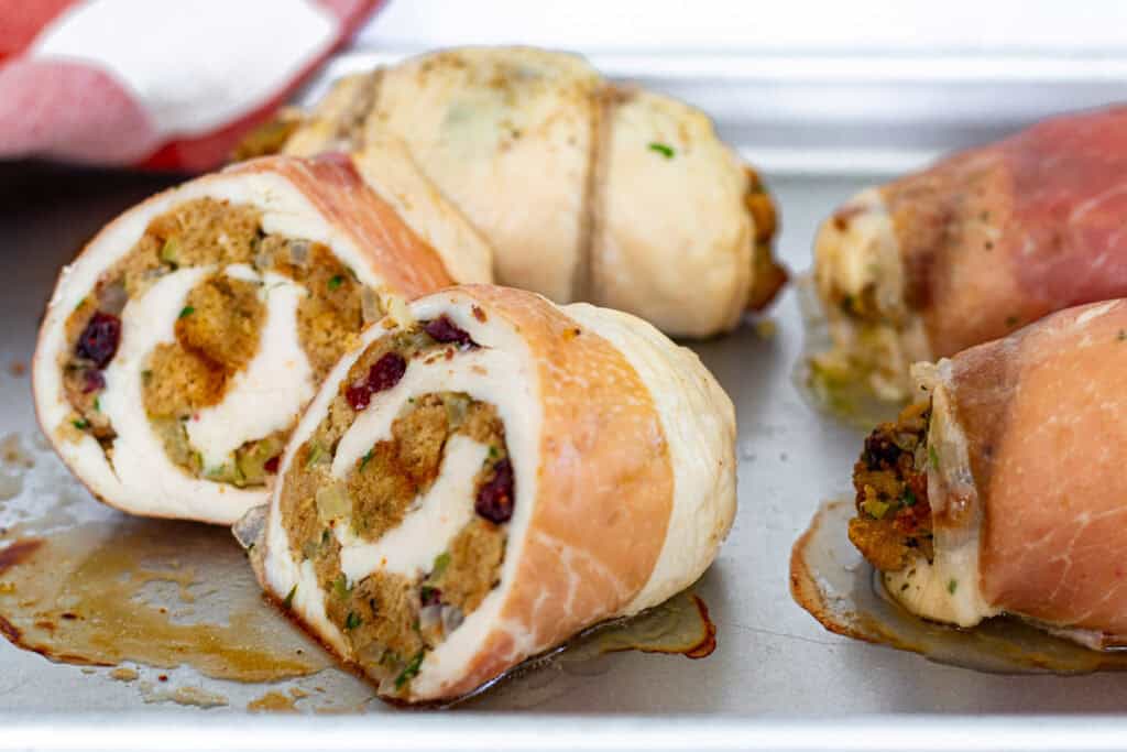 Baked stuffed chicken breast with stuffing sliced open to reveal layers of chicken, stuffing, and cranberries.