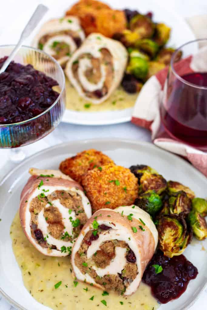 Plates of stuffed chicken breast with stuffing, gravy, roasted Brussels sprouts, and cranberry sauce for Thanksgiving dinner for two.