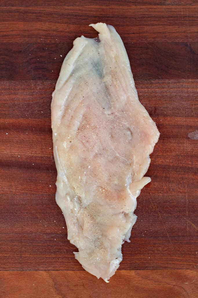 Butterflied chicken breast seasoned with salt, onion powder, and pepper, ready to be filled with stuffing.
