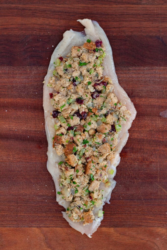 Chicken breast laid flat on a cutting board and topped with homemade bread stuffing mixture.