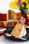 Slice of moist mini spiced apple cake showing apple chunks, served on black plate