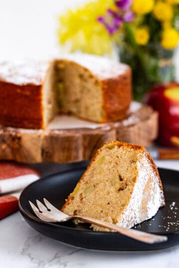 Slice of moist mini spiced apple cake showing apple chunks, served on black plate