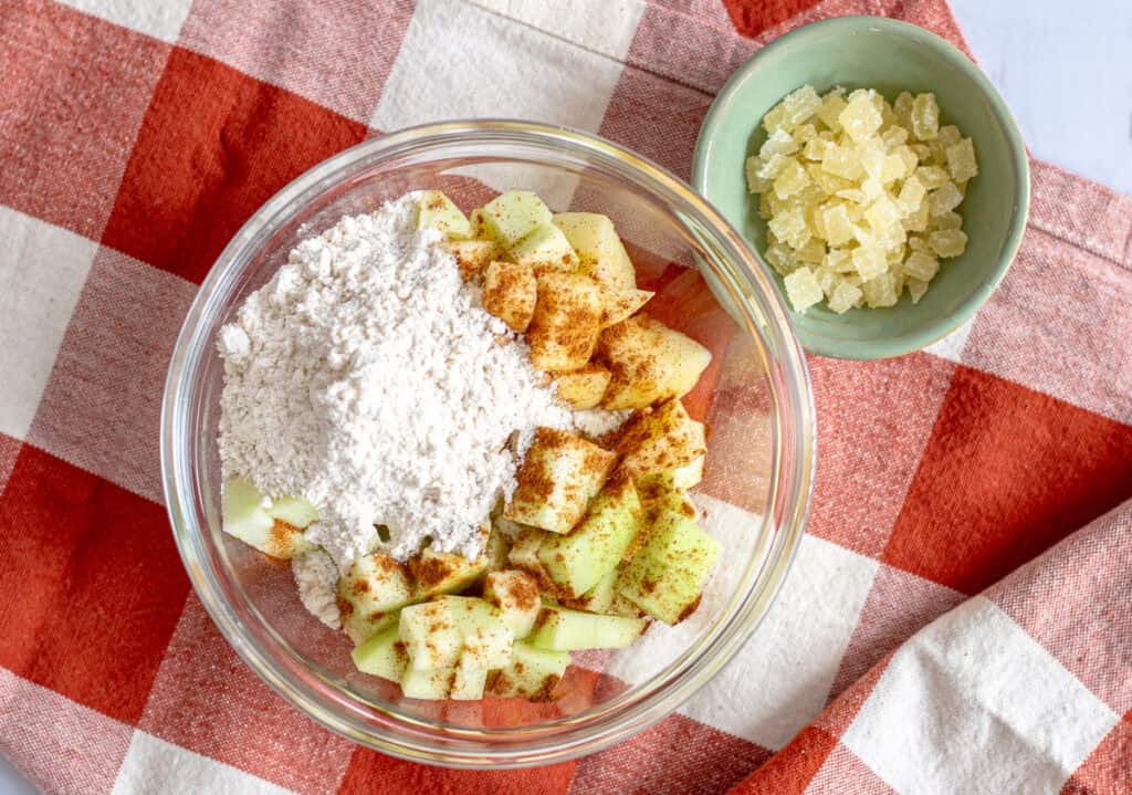 Diced apples tossed with flour and cinnamon for mini spiced apple cake, with candied ginger on the side