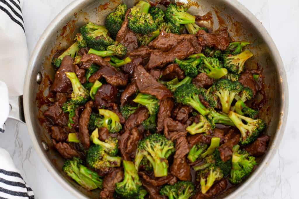 Beef and broccoli coated evenly in glossy stir fry sauce in a stainless steel skillet.