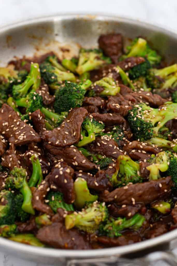 Finished beef and broccoli stir-fry in skillet sprinkled with toasted sesame seeds, ready to serve.
