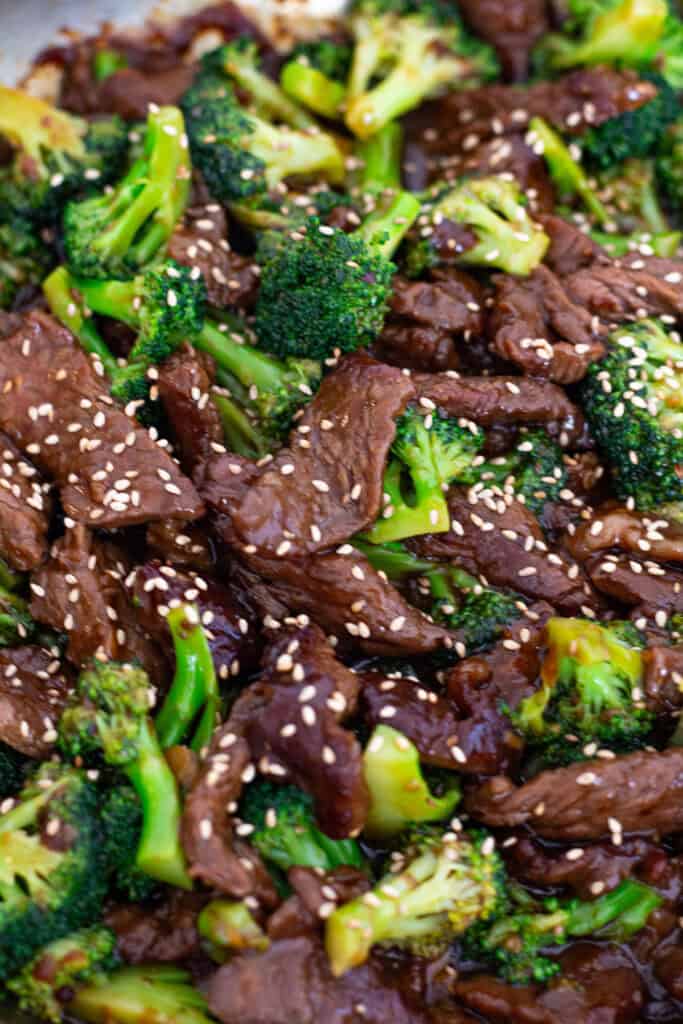 Close-up of tender beef and bright broccoli florets coated in glossy sauce with sesame seeds on top.