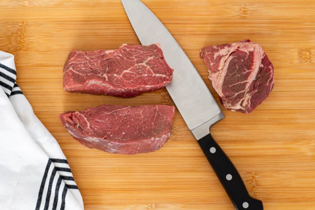 Top sirloin cut into medium chunks on a board with a chef’s knife, first step before slicing for beef and broccoli.