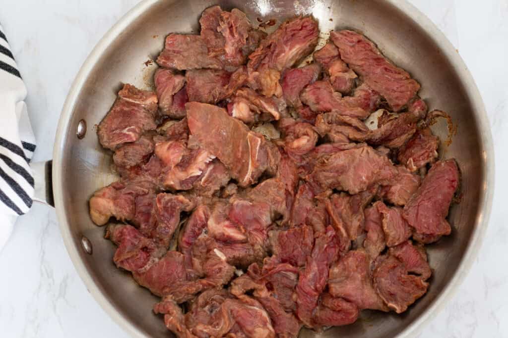 Thinly sliced beef searing in a hot skillet, beginning to brown on the edges for beef and broccoli stir fry.