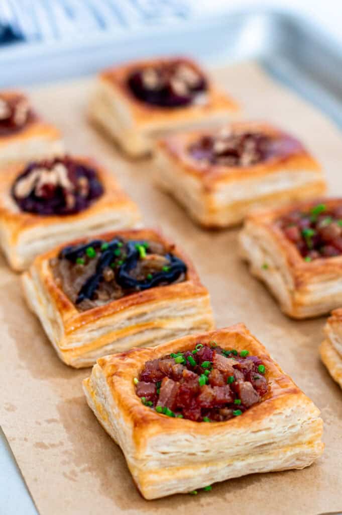 Golden puff pastry brie bites baking on a parchment-lined sheet pan with sweet and savory fillings.