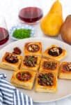 Plate of puff pastry brie bites served four ways with wine and pears in the background.