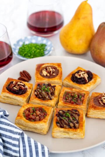 Plate of puff pastry brie bites served four ways with wine and pears in the background.