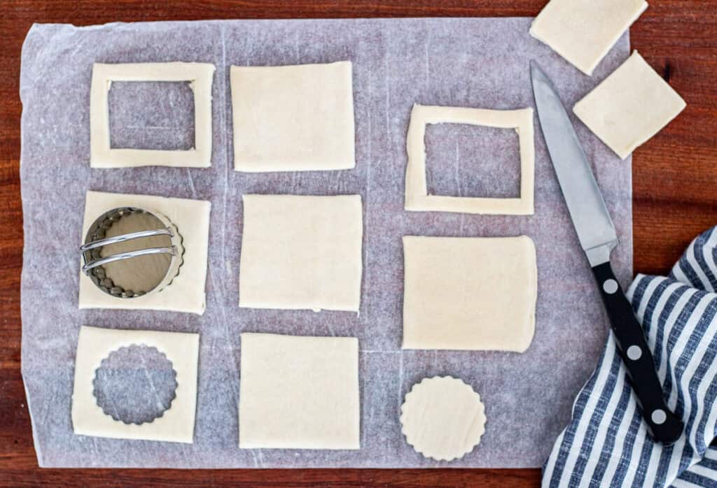 Puff pastry squares with center cutouts using a round and a square with a pairing knife to form vol-au-vent shapes.