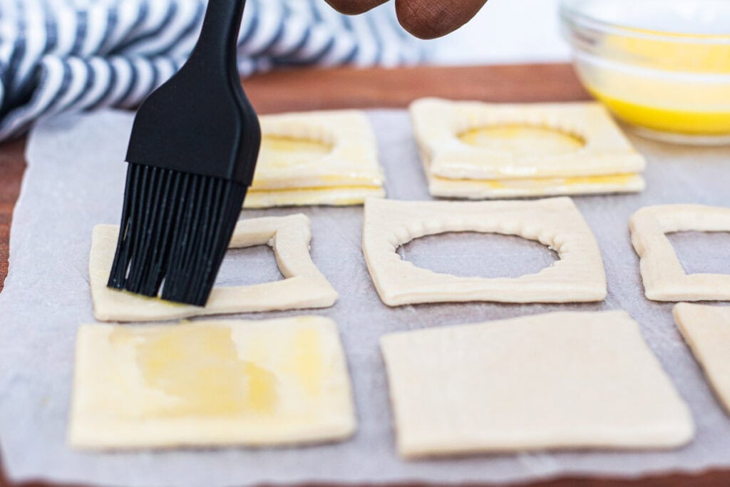 Brushing puff pastry tops with egg wash to glue the top piece and to help create a golden color.