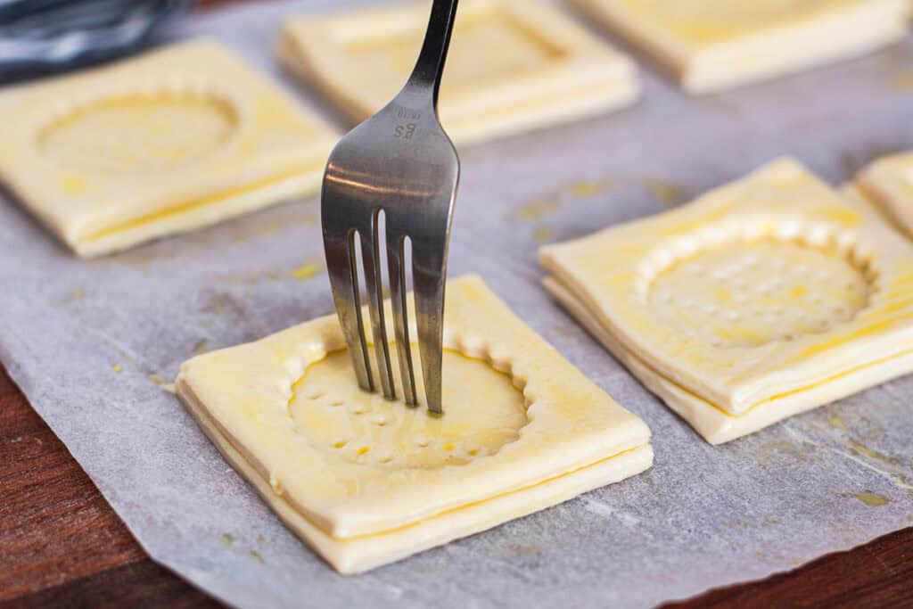 Fork pricking puff pastry centers to prevent over-puffing while baking vol-au-vent cases.