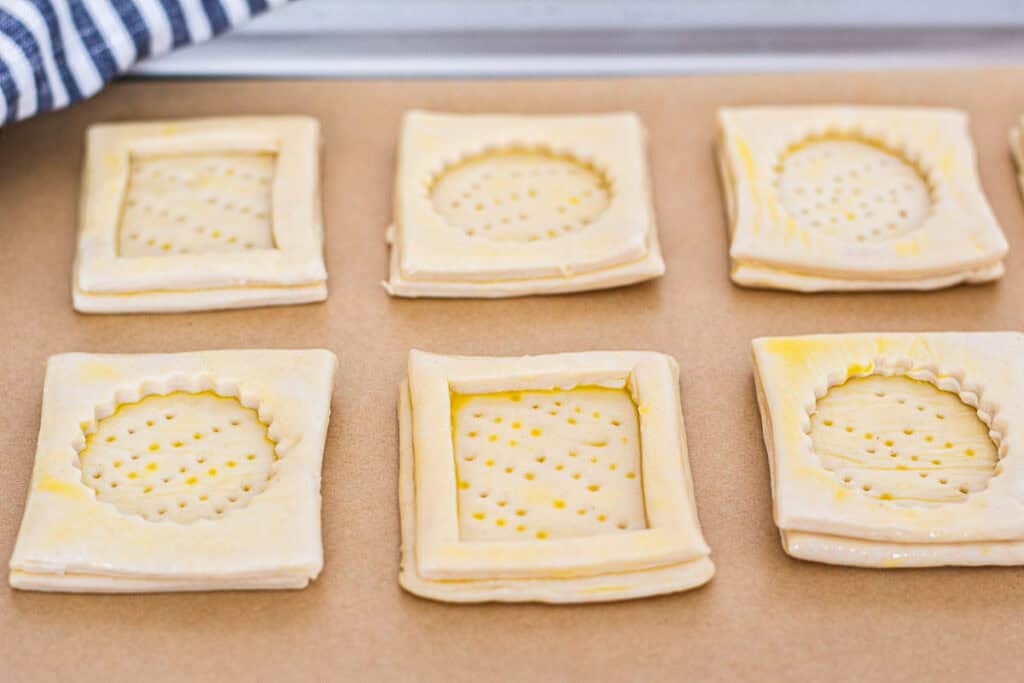 Prepared puff pastry vol-au-vent shells on parchment paper, brushed with egg wash and ready for the oven.