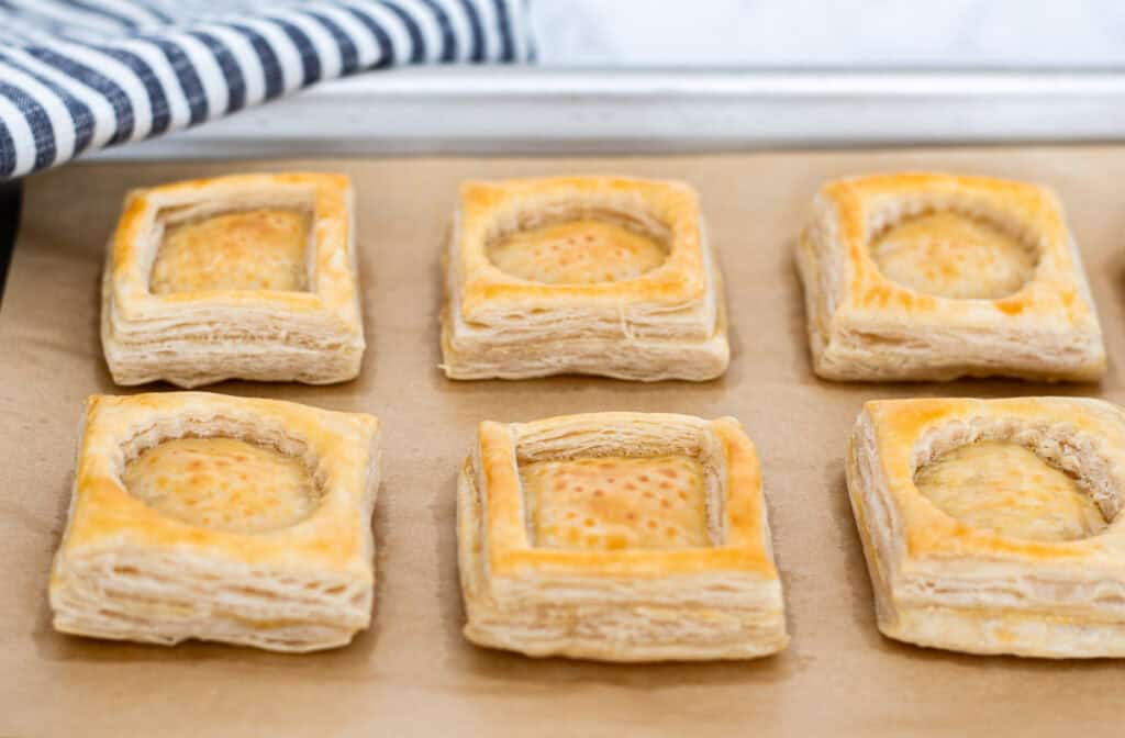 Golden baked puff pastry shells cooling on a baking sheet, showing crisp flaky layers.