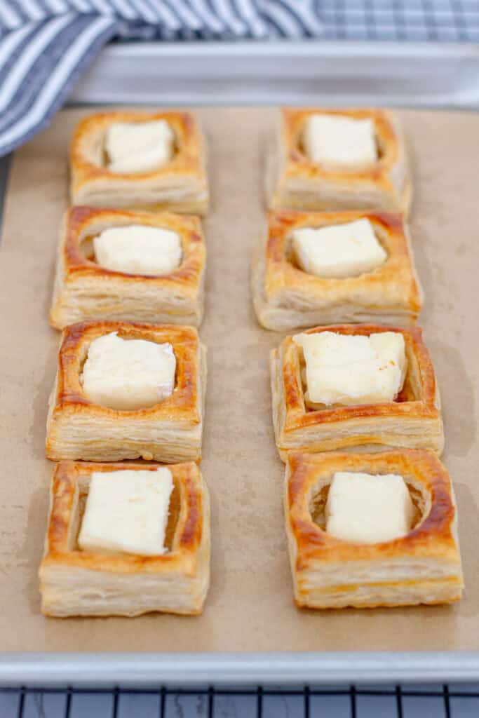 Baked puff pastry shells filled with small pieces of brie cheese before the final bake.