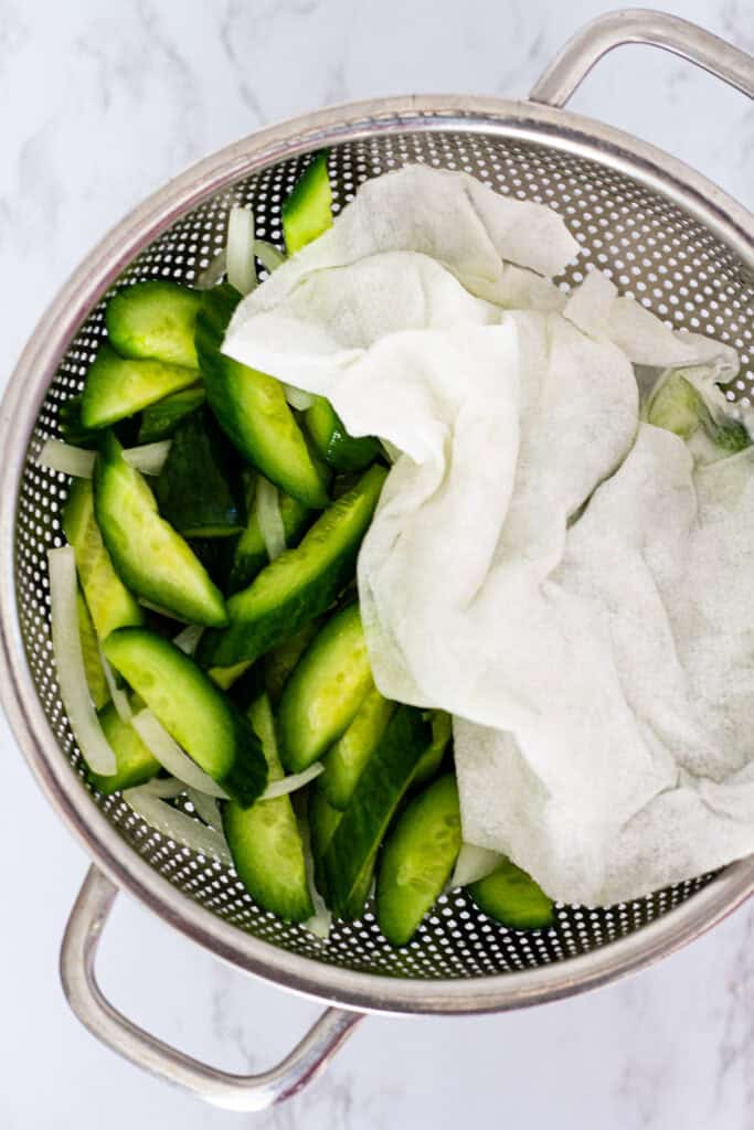 Cucumbers and onions being patted dry with paper towels before mixing the Korean cucumber salad dressing.