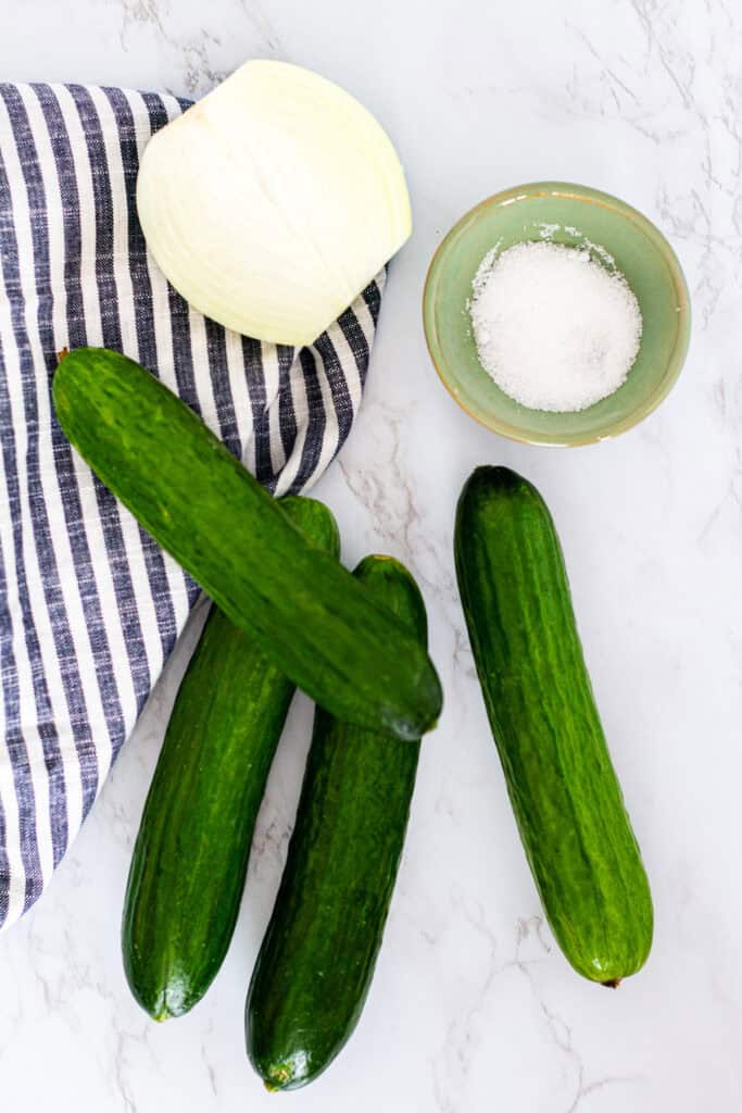 Persian cucumbers, onion, and salt displayed on a striped towel before making Korean cucumber salad.