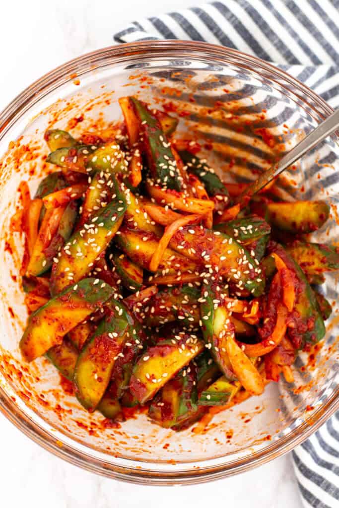 Korean cucumber salad fully mixed and garnished with sesame seeds in a glass bowl.