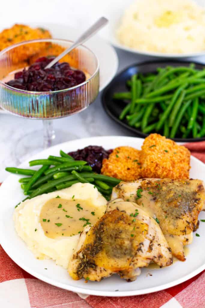 Plate of herb-butter chicken thighs with mashed potatoes, green beans, cranberry sauce, and gravy - an easy Thanksgiving dinner for two.