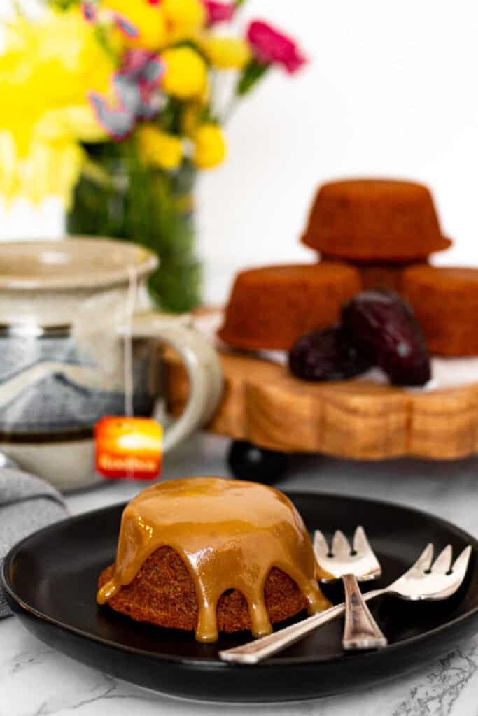 Mini sticky toffee pudding with warm toffee sauce drizzled on top and tea in background