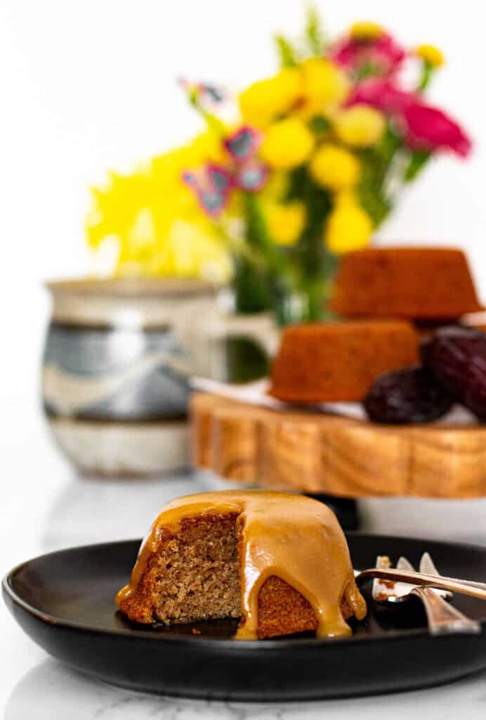 Mini sticky toffee pudding with bite taken, topped with toffee sauce and served with tea