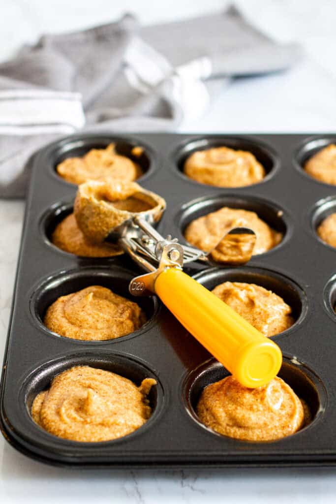 Scooping sticky toffee pudding batter into a muffin pan with yellow scoop