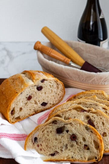 Slices of sourdough olive bread arranged on a kitchen towel, showing a golden crust and olive-studded interior.