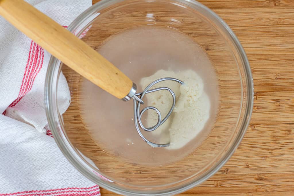 Sourdough starter dissolving into water in a glass bowl before adding flour