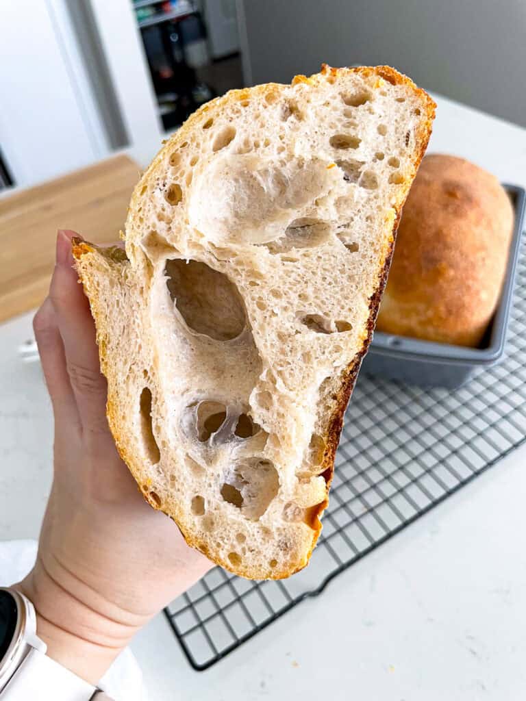 Slice of sourdough bread showing uneven crumb and large holes, a common result for sourdough beginners learning bulk fermentation.