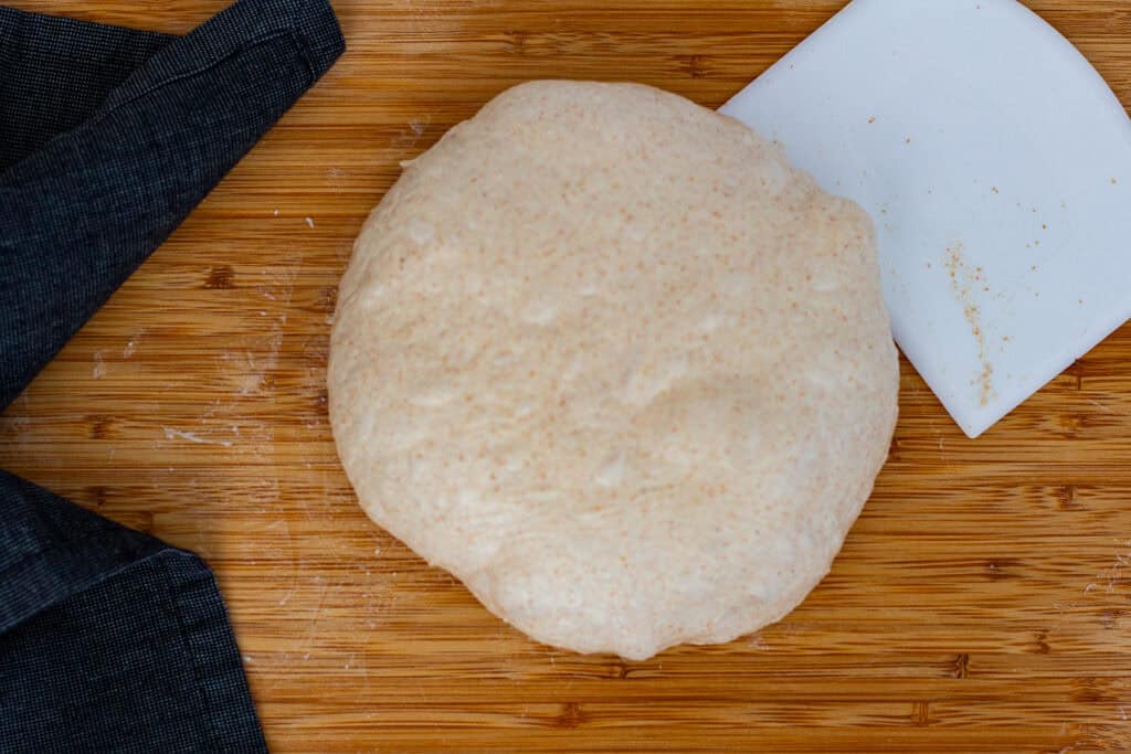 Flipped dough being shaped into a round using an upward swiping motion to create surface tension.