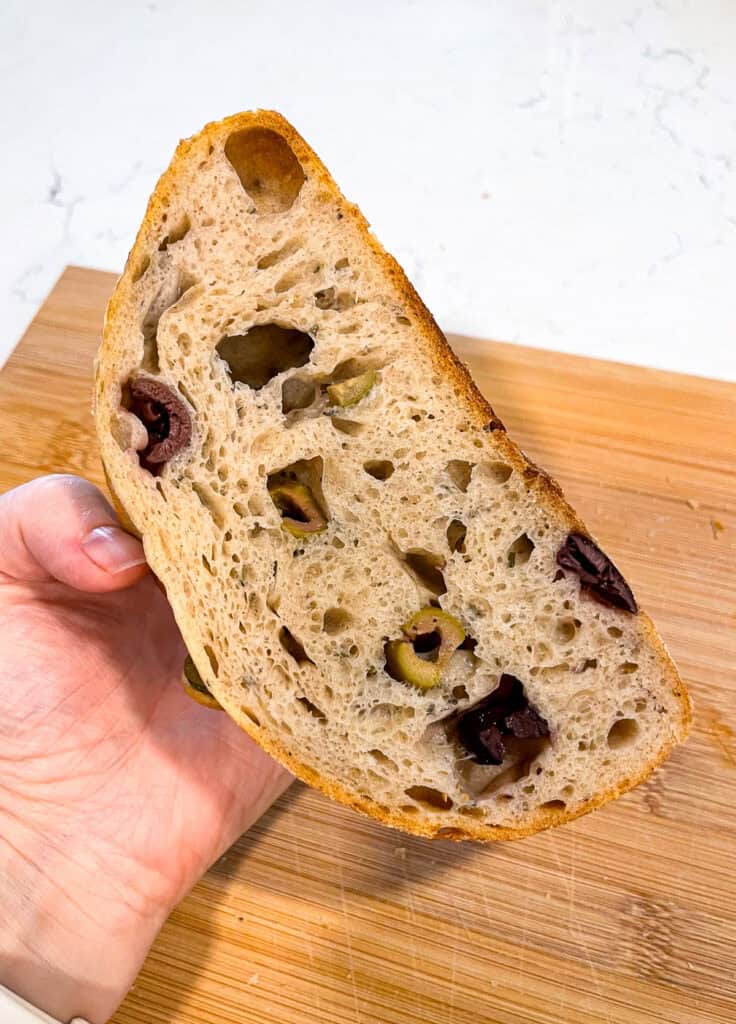 Slice of olive-studded sourdough bread with open crumb, showing an inclusion loaf made after gaining sourdough beginner confidence.