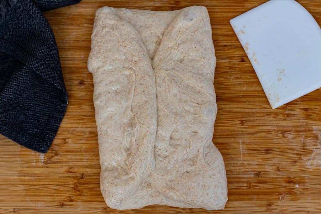 Dough folded from both sides toward the center during sourdough discard bread shaping.