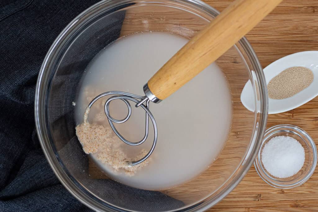 Sourdough discard being mixed into water before adding yeast and salt to make the dough.