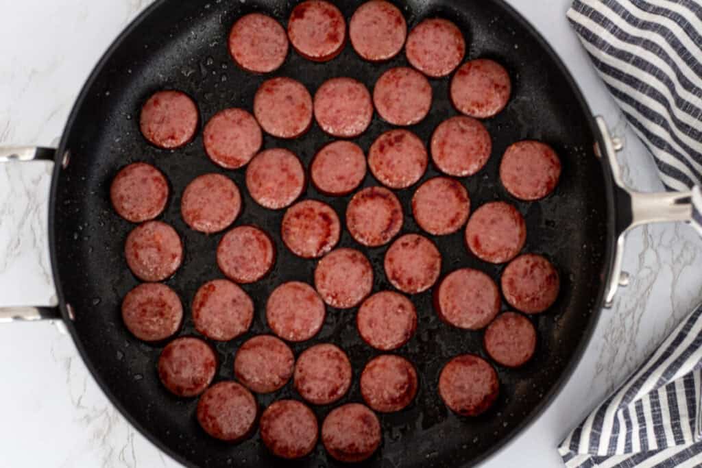Sliced sausage browning in a single layer in a skillet for Cajun sausage and shrimp stew.