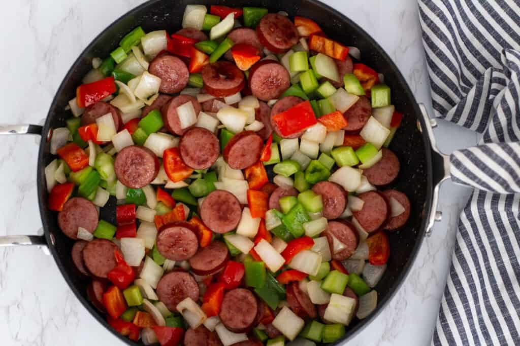 Sliced sausage sautéed with onions, celery, and bell peppers in a skillet.