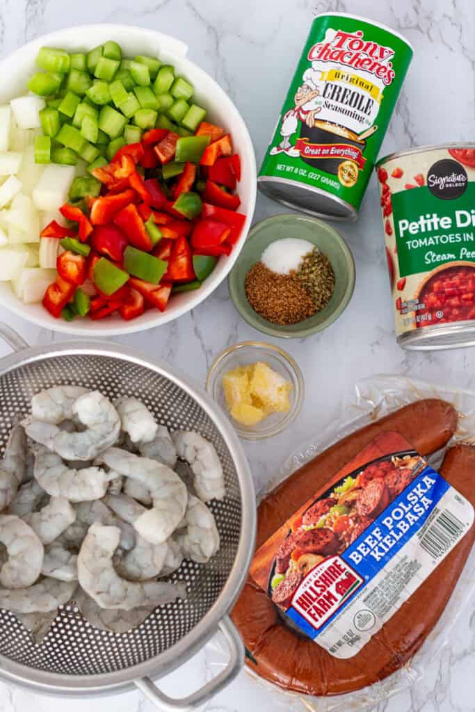Ingredients for Cajun sausage and shrimp stew, including chopped onions, celery, bell peppers, spices, tomatoes, raw shrimp, and kielbasa sausage.