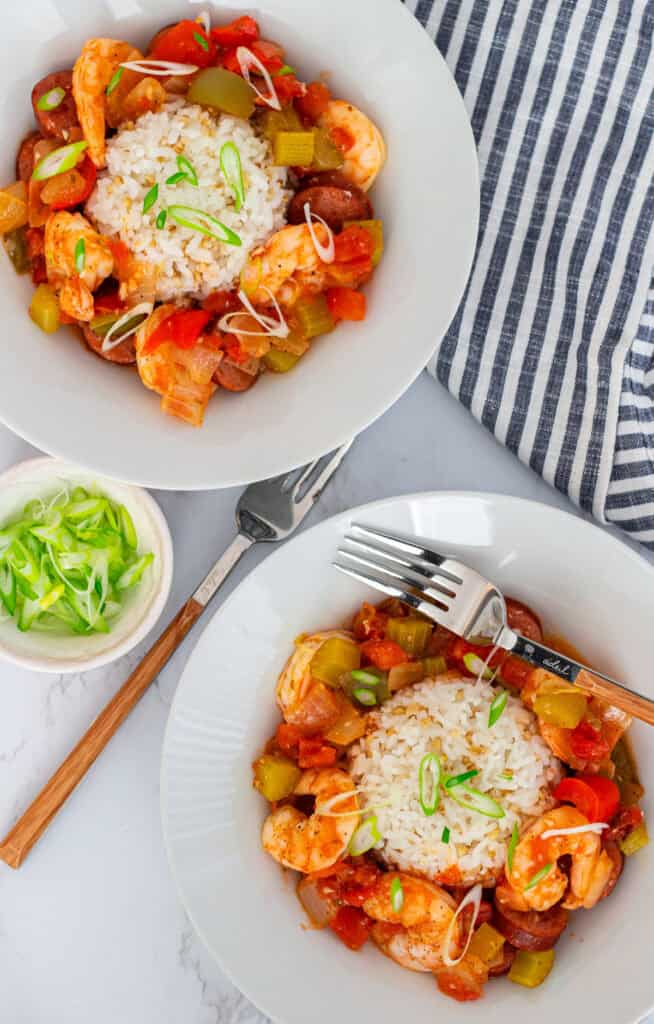 Two bowls of Cajun sausage and shrimp stew with rice and green onions, ready to serve.