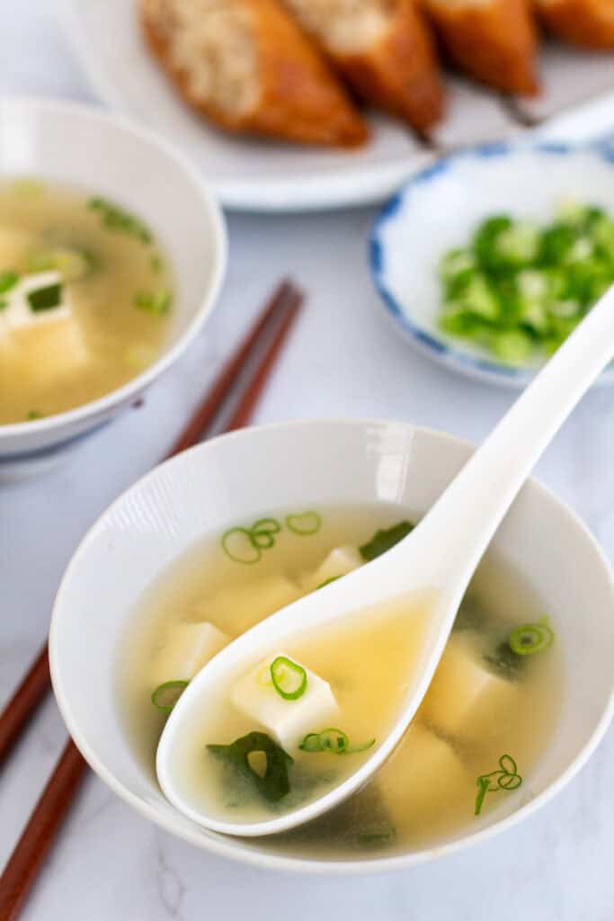 Spoonful of miso soup with tofu, wakame seaweed, and scallions in a light broth