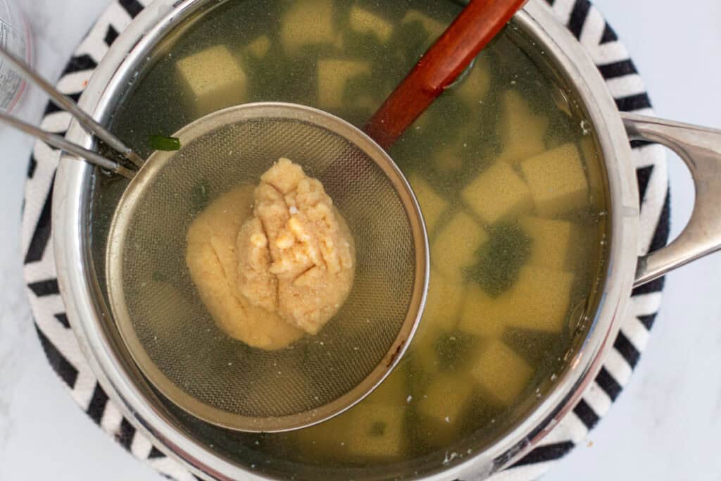Miso paste being gently dissolved into hot dashi using a mesh strainer